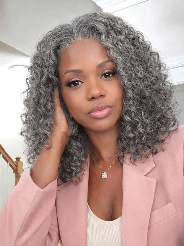 Front view with slight side angle of a medium-length salt and pepper gray wig with loose water wave curls, worn by a young real model, made of 100% human hair, ideal for natural, elegant everyday styling