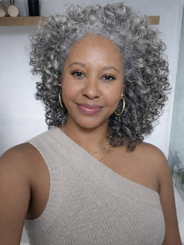 Black woman wearing salt and pepper bouncy curls glueless 100% human hair grey wig, natural soft curly texture, realistic short grey hairstyle for elegant and confident women.