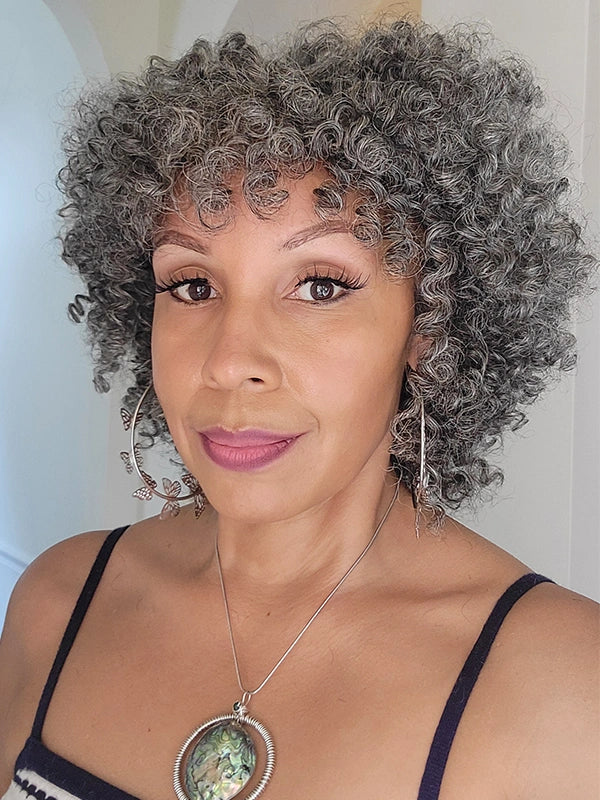 A woman wearing a realistic salt and pepper ringlet curls wig with bangs, showcasing natural-looking hair with curls and a stylish appearance.